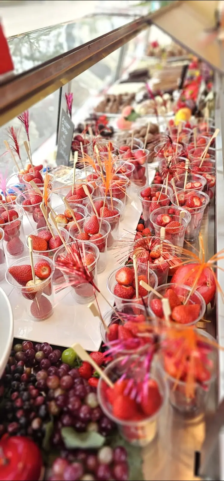 Becher mit frischen Erdbeeren und Spieße mit glasierten Früchten in der Auslage