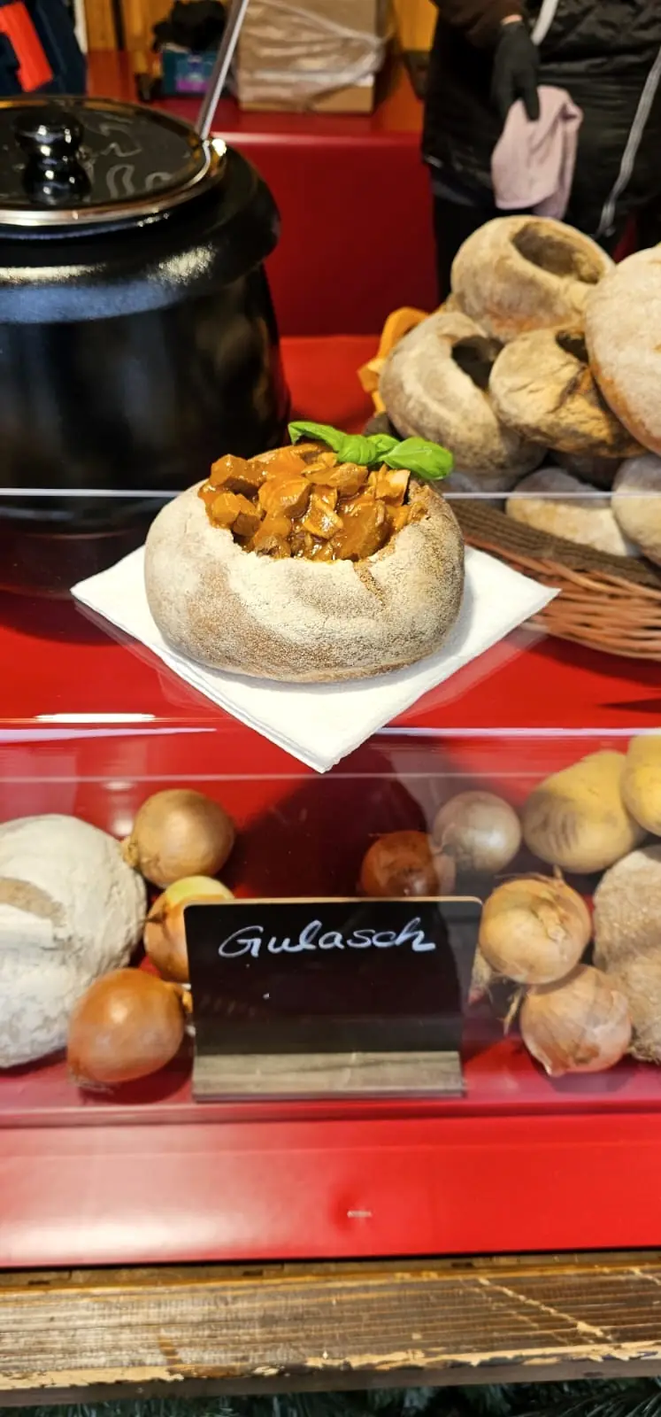 Gulaschsuppe im Brotlaib auf der roten Theke, daneben der Kessel