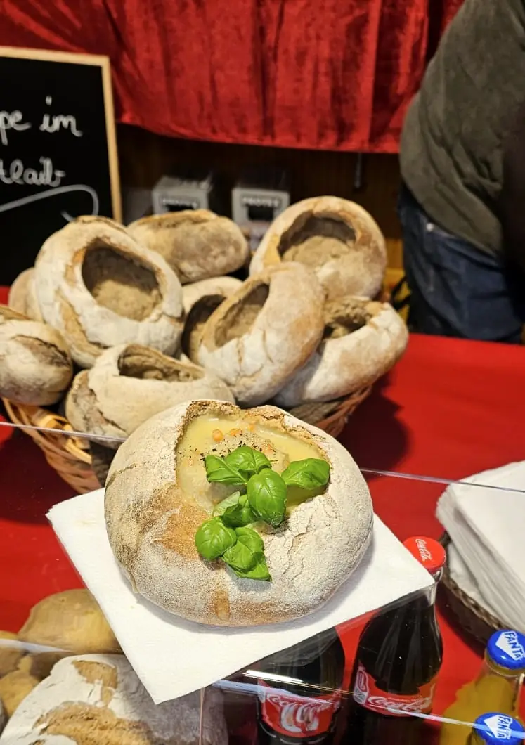 Suppe im Brotlaib mit frischem Basilikum, dahinter der Korb mit den Laiben