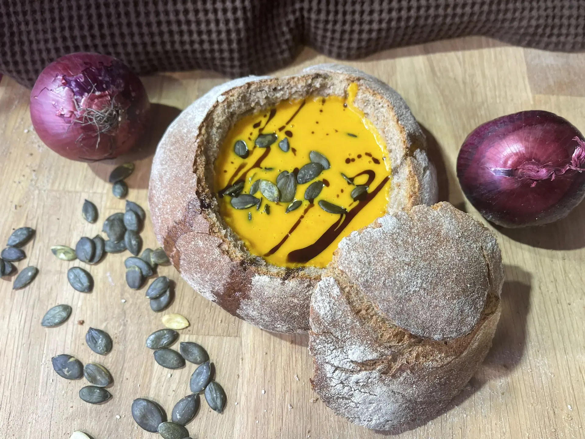 Kürbissuppe im ausgehöhlten Brotlaib, daneben rote Zwiebeln