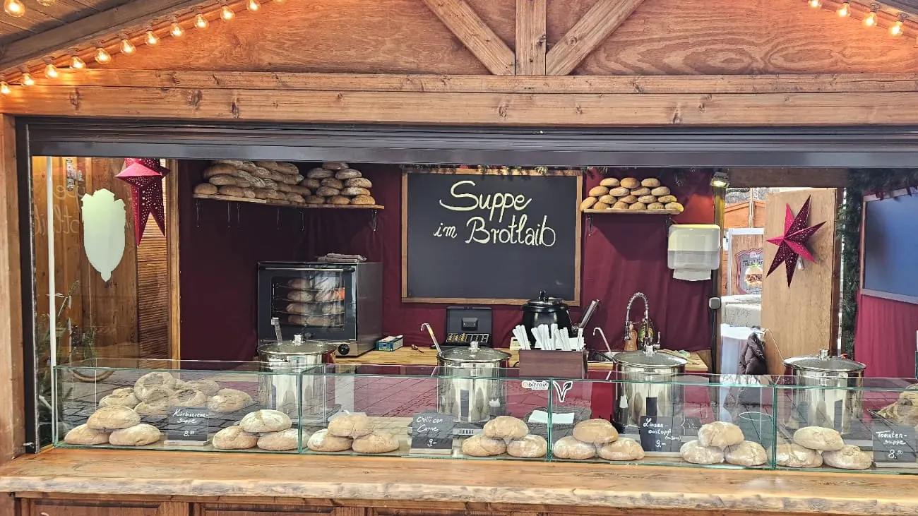 Die Holzhütte mit der Tafel Suppe im Brotlaib, dahinter die vorbereiteten Laibe