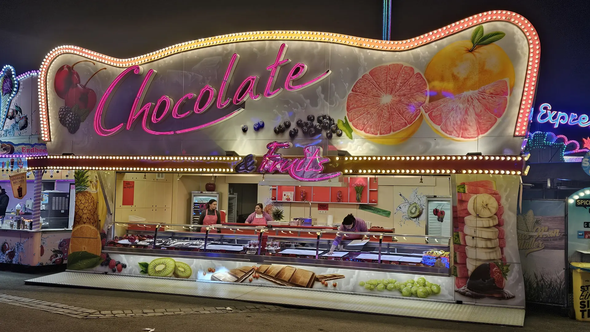 Der Wagen Chocolate & Fruits bei Nacht, der pinke Neonschriftzug leuchtet über der Theke